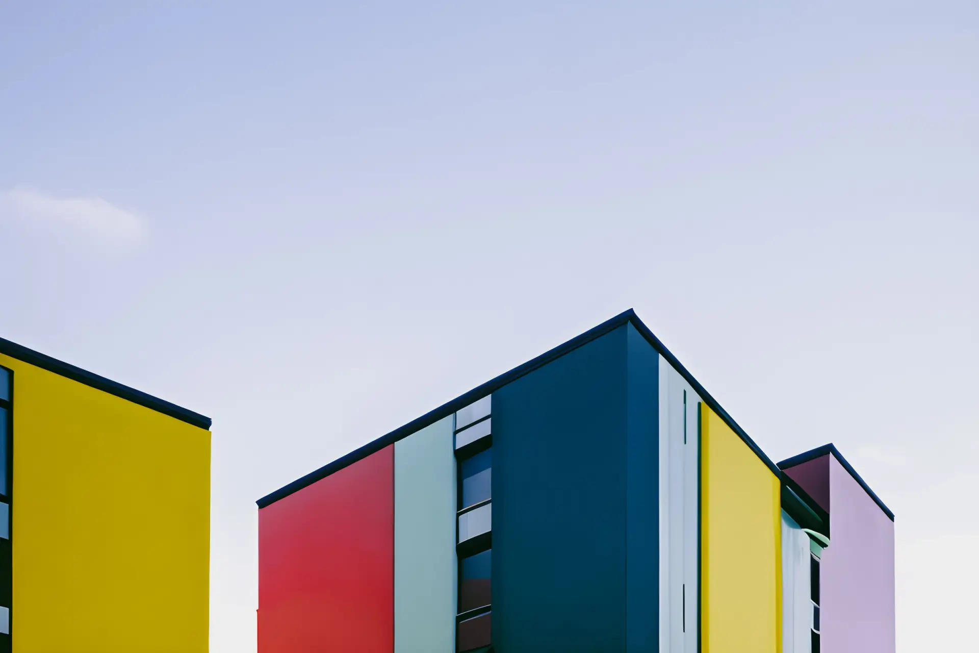 Immeubles modernes aux façades en aplats jaune, rouge, bleu et lilas sous un ciel clair