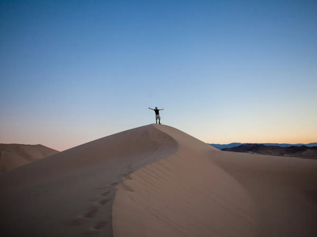 Silhouette lointaine, bras levés, au sommet d'une dune