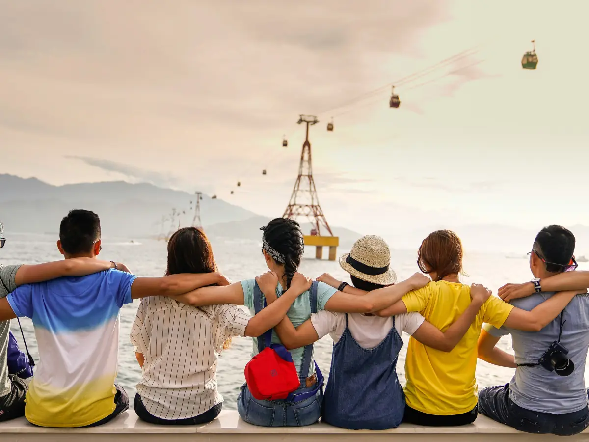 Groupe d'amis vus de dos, bras sur les épaules, assis face à la mer