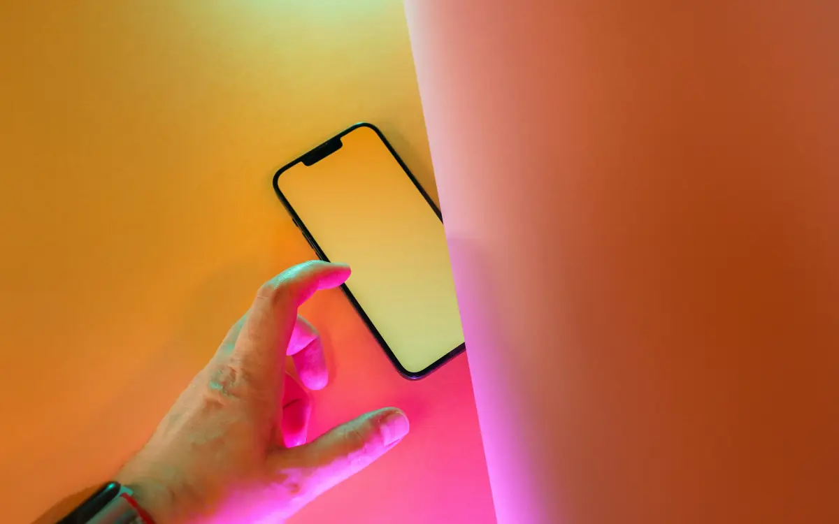 Main tenant un téléphone près d'un mur orange et rose