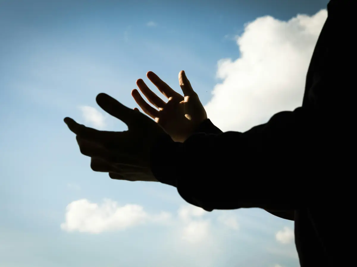 Mains ouvertes en silhouette devant un ciel bleu et des nuages