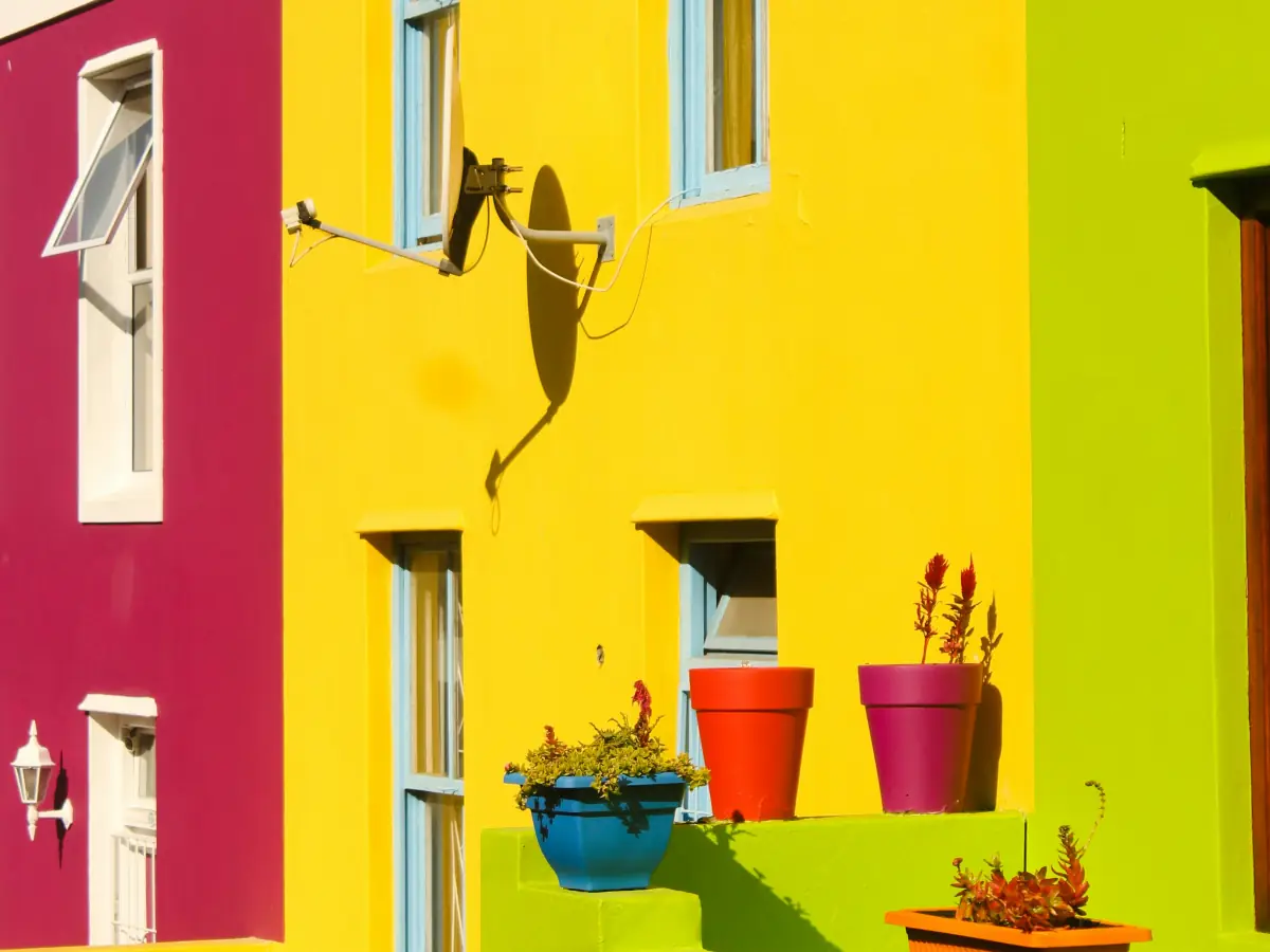 Maisons jaune, magenta et vert lime avec pots de fleurs au soleil